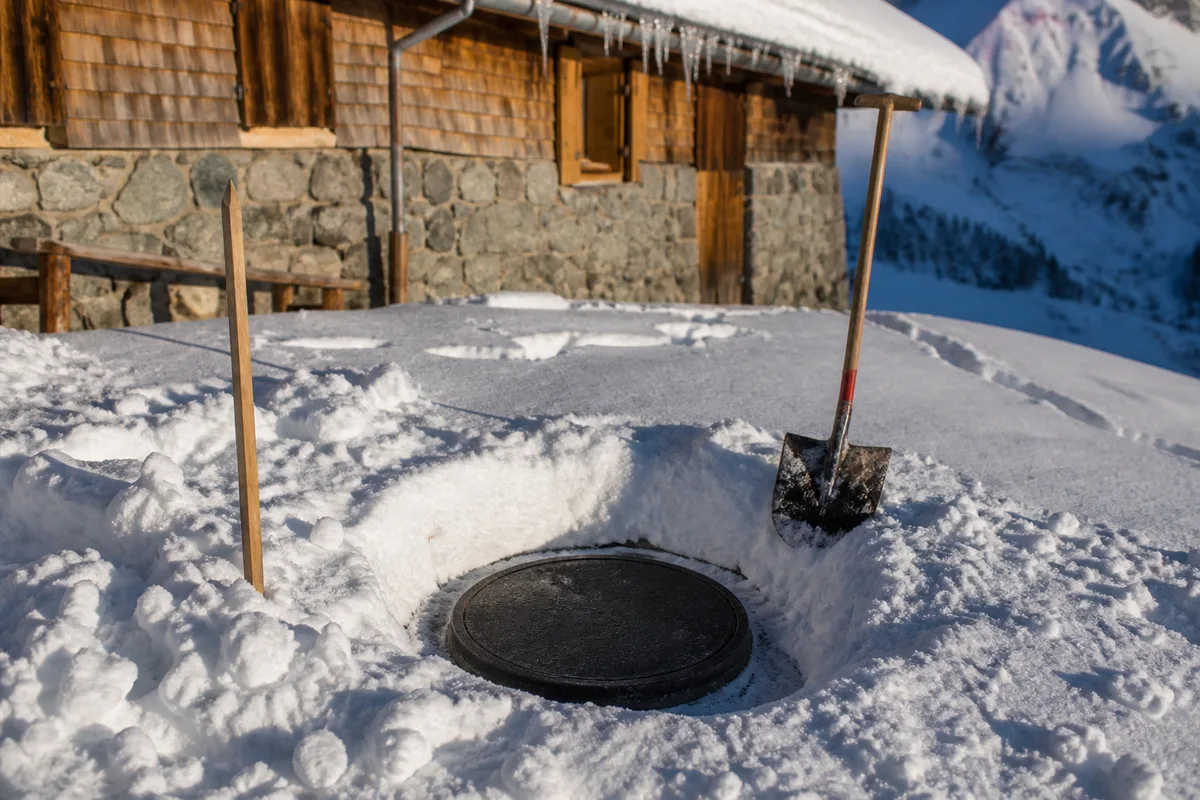 Regard d’assainissement dégagé à la pelle dans la neige tassée devant un chalet savoyard