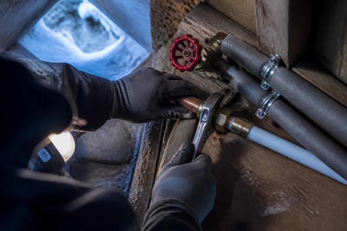Mains gantées reprenant un raccord entre un tube de cuivre ancien et du multicouche dans un chalet