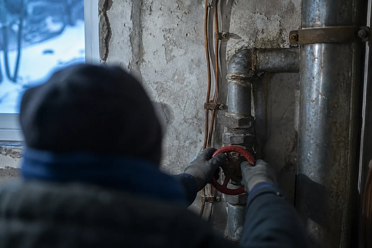 Mains gantées refermant une vanne d’arrêt dans un local technique d’immeuble ancien du plateau d’Assy